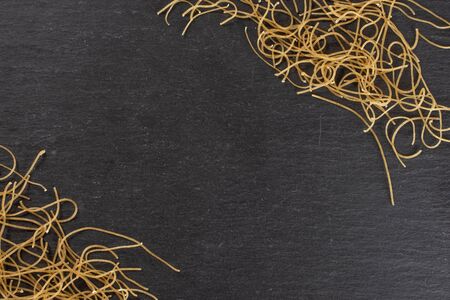 Lot of pieces of thin raw pasta noodles copyspace in middle flatlay on grey stoneの写真素材