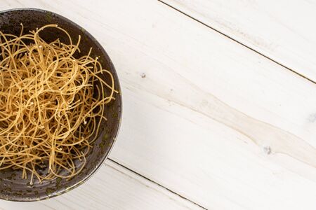 Lot of pieces of thin raw pasta noodles copyspace on right on grey ceramic plate flatlay on white...