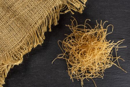 Lot of pieces of thin raw pasta noodles with jute cloth flatlay on grey stone