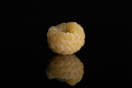 One whole ripe fresh golden hymalayan raspberry isolated on black glass