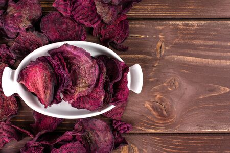 Lot of slices of dried red beetroot in white oval ceramic bowl flatlay on brown woodの写真素材