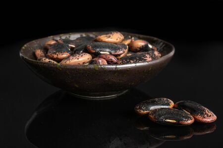 Lot of whole stained purple bean in dark ceramic bowl isolated on black glassの写真素材