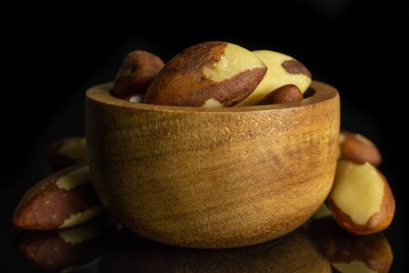 Lot of whole raw brown brazil nut in tiny wooden bowl isolated on black glassの写真素材