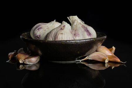 Group of three whole lot of pieces of organic white garlic allium sativum in dark ceramic bowl isolated on black glassの写真素材