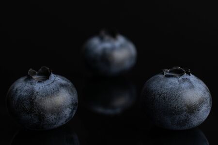 Group of three whole fresh blue bilberry isolated on black glassの写真素材