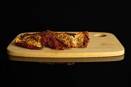 Lot of whole dried red tomato on bamboo cutting board isolated on black glassの写真素材