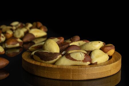 Lot of whole raw brown brazil nut on bamboo coaster isolated on black glassの写真素材