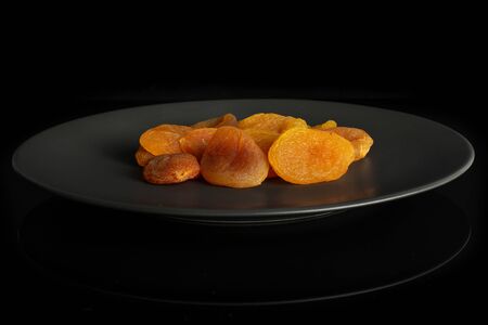 Lot of whole dried orange apricot on gray ceramic plate isolated on black glassの写真素材