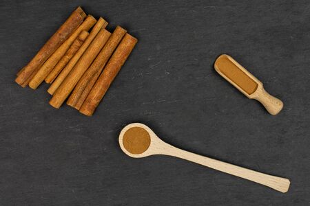 Lot of whole dry brown cinnamon in a wooden spoon in a wooden scoop flatlay on grey stoneの写真素材