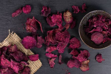 Lot of slices of dried red beetroot on natural sackcloth in dark ceramic bowl flatlay on grey stoneの写真素材