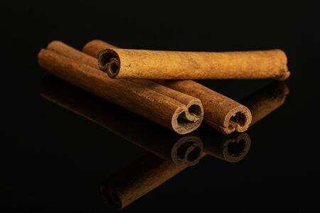 Group of three whole dry brown cinnamon isolated on black glassの写真素材