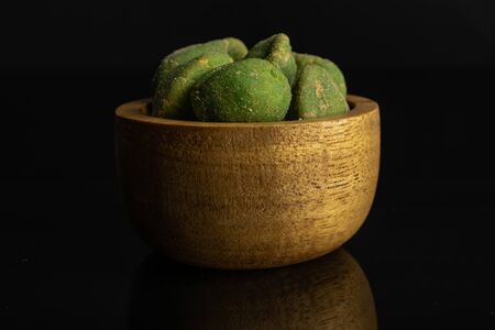 Lot of whole spicy green wasabi peanut in tiny wooden bowl isolated on black glassの写真素材