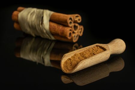 Group of six whole dry brown cinnamon wrapped in natural bast in a wooden scoop isolated on black...