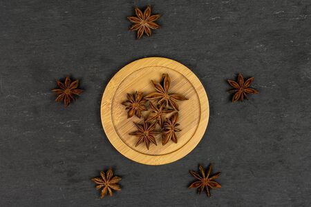 Lot of whole dry brown star anise illicium verum on round bamboo coaster flatlay on grey stone