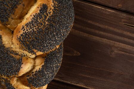 One whole twisted poppy seed bun flatlay on brown woodの写真素材