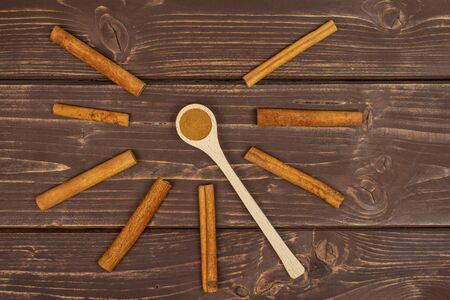 Group of eight whole dry brown cinnamon in a wooden spoon flatlay on brown woodの写真素材