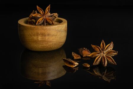 Group of lot of whole four pieces of dry brown star anise illicium verum in tiny wooden bowl isolated on black glassの写真素材