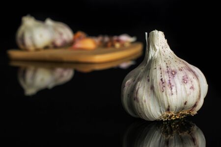 Group of three whole lot of pieces of organic white garlic allium sativum on bamboo cutting board isolated on black glassの写真素材