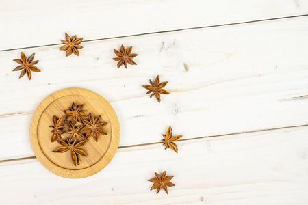 Lot of whole dry brown star anise illicium verum on round bamboo coaster flatlay on white woodの写真素材