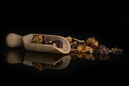 Lot of pieces of lingonberry strawberry fruit tea pieces with wooden scoop isolated on black glassの写真素材