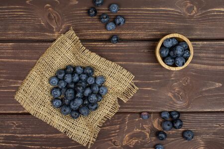 Lot of whole fresh blue bilberry in tiny wooden bowl on natural sackcloth flatlay on brown woodの写真素材