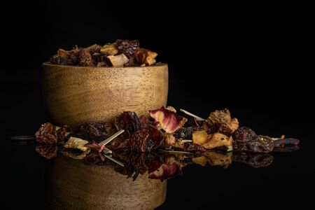 Lot of pieces of lingonberry strawberry fruit tea pieces in wooden bowl isolated on black glass
