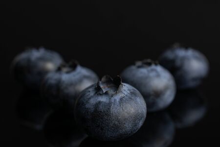 Group of five whole fresh blue bilberry isolated on black glassの写真素材