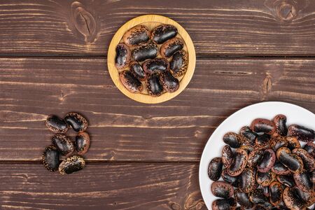 Lot of whole stained purple bean on round bamboo coaster on white ceramic plate flatlay on brown...