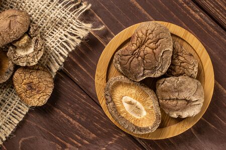 Lot of whole dry mushroom shiitake on bamboo plate on jute cloth flatlay on brown woodの写真素材