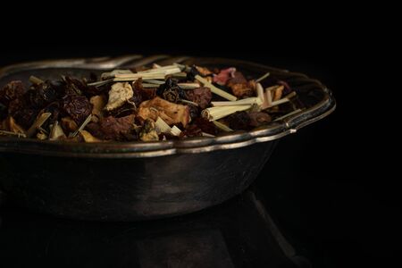 Lot of pieces of lingonberry strawberry fruit tea in old iron bowl isolated on black glass