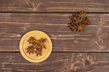 Lot of whole dry brown star anise illicium verum on round bamboo coaster flatlay on brown woodの写真素材