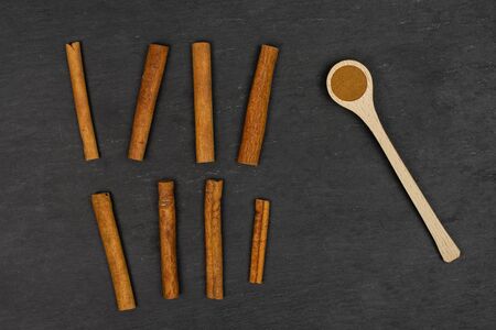 Group of eight whole dry brown cinnamon in a wooden spoon flatlay on grey stoneの写真素材