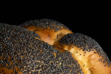 Closeup of one whole twisted poppy seed bun macro isolated on black glassの写真素材