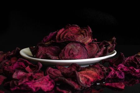 Lot of slices of dried red beetroot on white ceramic plate isolated on black glassの写真素材