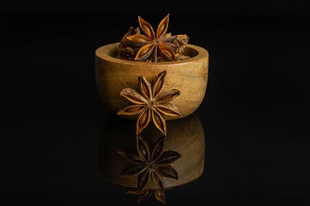 Lot of whole dry brown star anise illicium verum in tiny wooden bowl isolated on black glassの写真素材