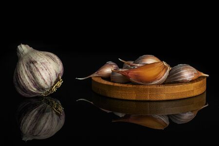 One whole lot of pieces of organic white garlic allium sativum on bamboo coaster isolated on black glassの写真素材