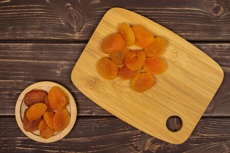 Lot of whole dried orange apricot on round bamboo coaster on bamboo cutting board flatlay on brown woodの写真素材