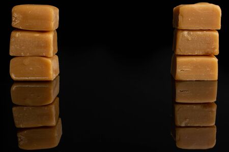 Group of six whole sweet golden caramel candy in two columns isolated on black glassの写真素材