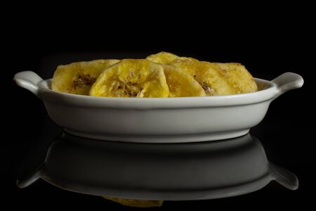 Lot of slices of sweet yellow dry banana in white oval ceramic bowl isolated on black glassの写真素材