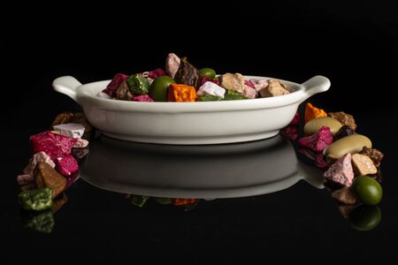 Lot of whole sweet chocolate stone in white oval ceramic bowl isolated on black glass