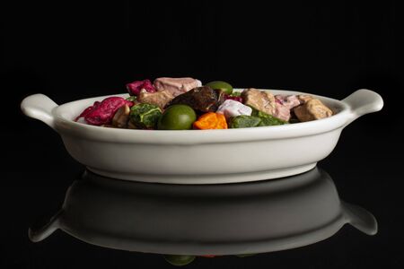 Lot of whole sweet chocolate stone in white oval ceramic bowl isolated on black glassの写真素材