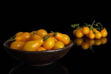 Lot of whole fresh yellow pear tomato in dark ceramic bowl isolated on black glassの写真素材