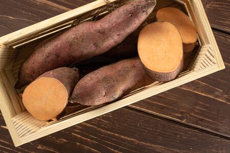Lot of whole lot of slices of fresh brown sweet potato with wooden crate flatlay on brown woodの写真素材