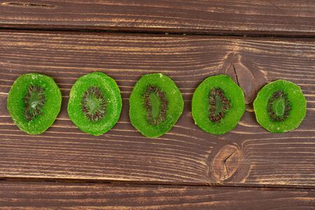 Group of five slices of sweet green candied kiwifruit flatlay on brown woodの写真素材