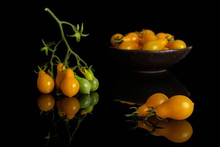Lot of whole fresh yellow pear tomato in dark ceramic bowl isolated on black glassの写真素材