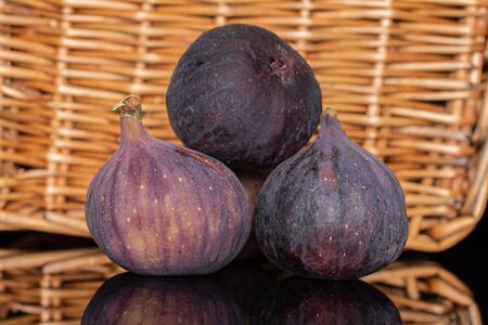 Group of three whole fresh fig fruit with braided rattan behind
