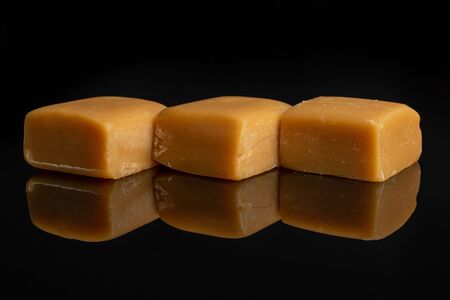 Group of three whole sweet golden caramel candy isolated on black glassの写真素材