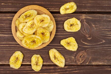 Lot of slices of sweet yellow dry banana on bamboo coaster flatlay on brown woodの写真素材