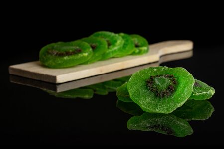 Group of eight slices of sweet green candied kiwifruit on small wooden cutting board isolated on black glassの写真素材