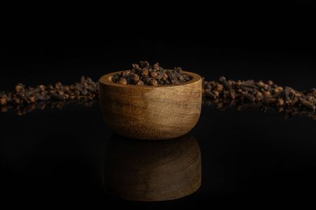 Lot of whole dry brown clove in tiny wooden bowl isolated on black glassの写真素材